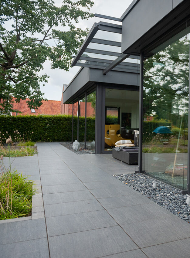 Gartenbau Nordhorn – moderne Terrassengestaltung mit Betonpflaster und Glasüberdachung von Holzquadrat