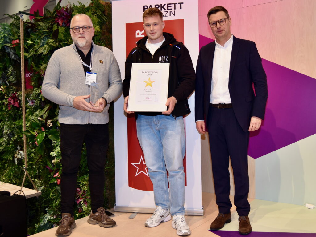 Übergabe des Parkett Star 2026 in der Kategorie "Vorbildlicher Generationswechsel" an Holzquadrat auf der Domotex: Manfred Reinink und Lucas Reinink nehmen Pokal und Urkunde entgegen